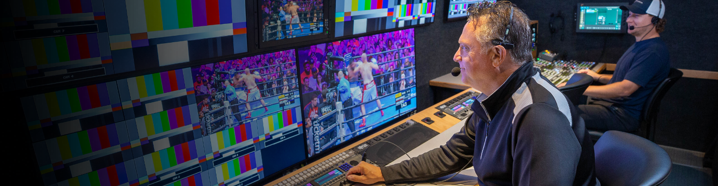 Man sitting in front of multiple computer monitors all showing a boxing match