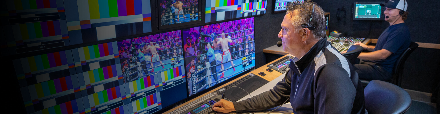 Un hombre sentado frente a múltiples monitores de computadora, todos muestran un combate de boxeo