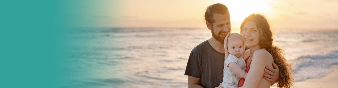 Un hombre, una mujer y un bebé sonriendo al atardecer en la playa