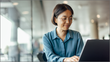 Woman on computer in office with large windows behind her