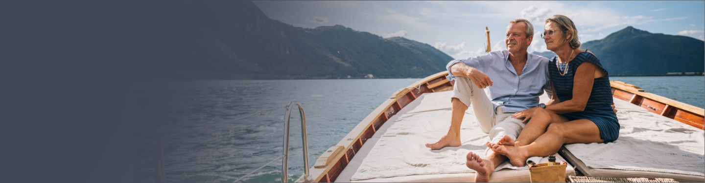 Un hombre y una mujer sentados juntos en un gran barco de lujo sobre el agua rodeados de montañas