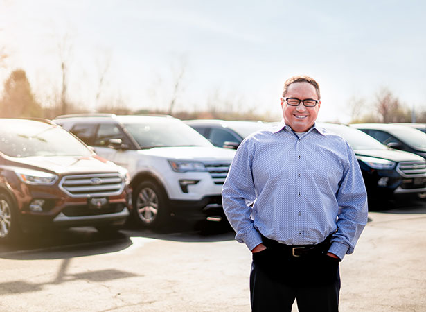 Keith Kocourek, president of Kocourek Automotive, stands in a parking lot in front of SUVs.