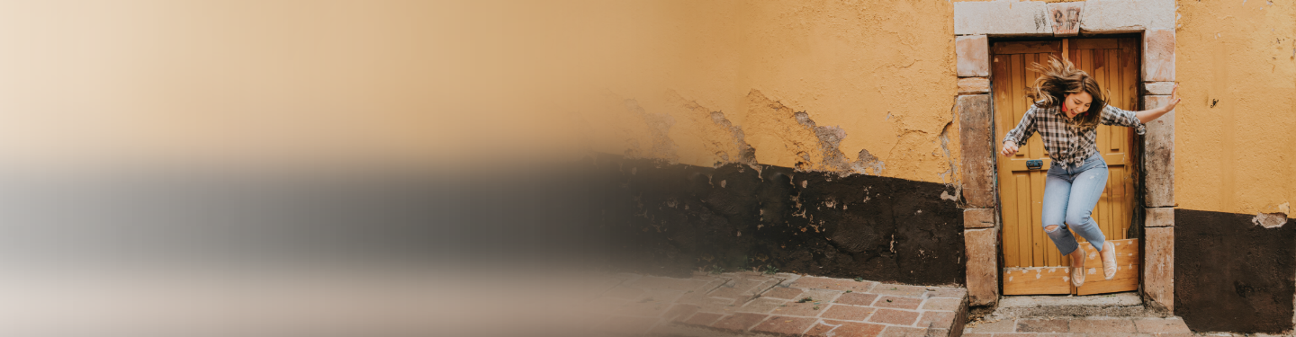 Mujer saltando de alegría frente a una puerta de madera rústica.