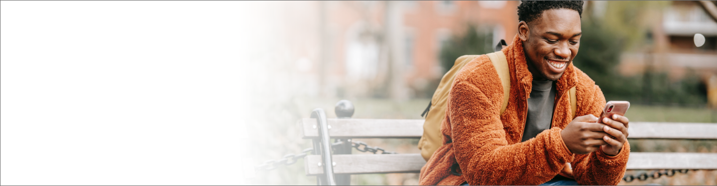 Man wearing backpack sitting on park bench smiling while looking at phone