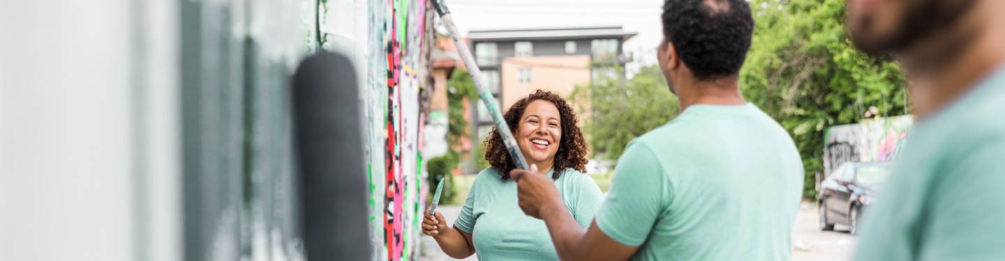 A woman smiling and looking at a man while they volunteer painting a wall.