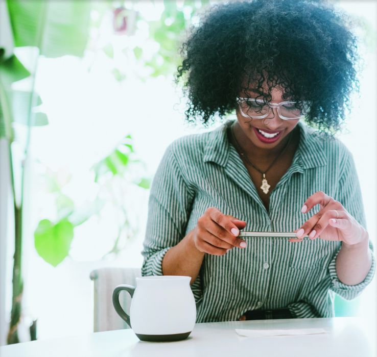 Woman in glasses and a mug next to her using mobile deposit to take a picture of a check.