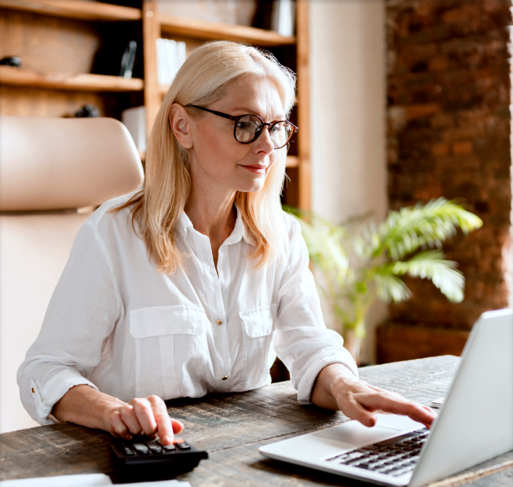Woman with glasses sitting at desk in office with laptop and calculator