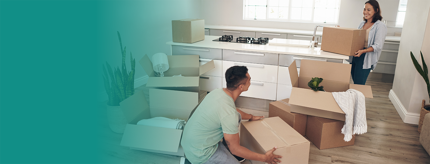 A young couple carries moving boxes into a kitchen.