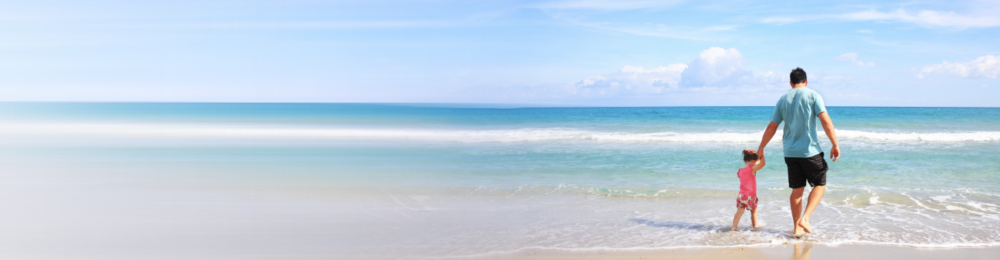 Man and young child walking in the water on a beach