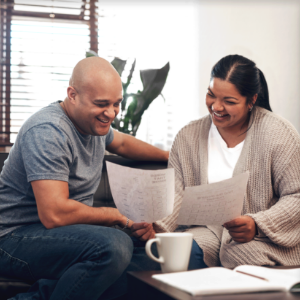 A man and woman smile while looking over paperwork in their living room.
