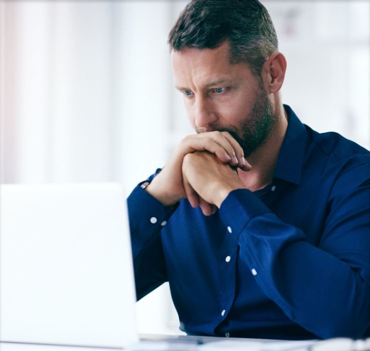 Man looking at laptop with hands together against his mouth